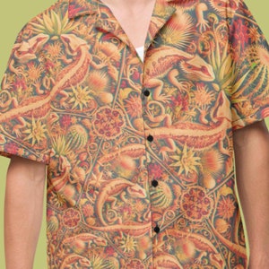 Peut inclure: Une chemise à manches courtes à boutons avec un motif coloré et complexe représentant des lézards et des motifs floraux. La chemise est faite d'un tissu léger et a une coupe décontractée.
