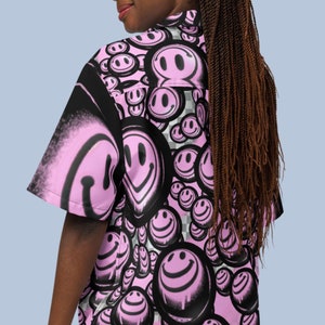 May include: A pink and black button-up shirt with a pattern of pink smiley faces. The shirt has short sleeves and a collared neckline.