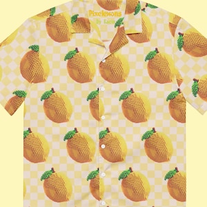 May include: A yellow short-sleeved button-up shirt with a checkered pattern and a pixelated lemon print. The shirt has a collar and a button closure. The text "Pixelemons by Kachi" is printed on the collar.