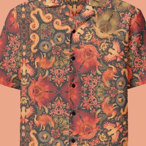 Può includere: Una camicia a maniche corte con bottoni e un motivo colorato e intricato che presenta creature mitiche, fiori e serpenti. La camicia ha un colletto e una chiusura con bottoni sul davanti. Il testo "Vrolijk Barbertje De Kat" è stampato sul colletto.