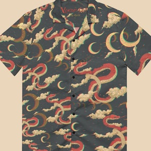 May include: A dark blue short-sleeved button-up shirt with a retro-style print of red and white snakes, crescent moons, and clouds. The shirt has a collar and a button-up front. The text "Visual Code by Kodie" is printed on the collar.