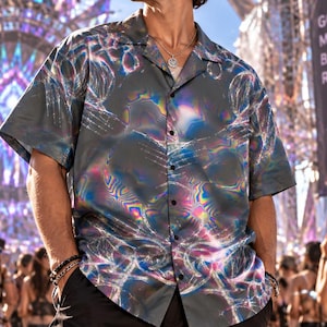 May include: A short-sleeved button-down shirt in a dark gray fabric featuring a holographic, iridescent swirling pattern. The shirt has a classic collar, a front button placket with black buttons, and a loose, relaxed fit worn with black cargo shorts.