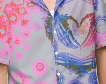 May include: Short-sleeved button-down shirt with a unique, colorful pattern. The shirt features a gray base with vibrant pink, blue, and purple abstract designs. The model is wearing light blue shorts.