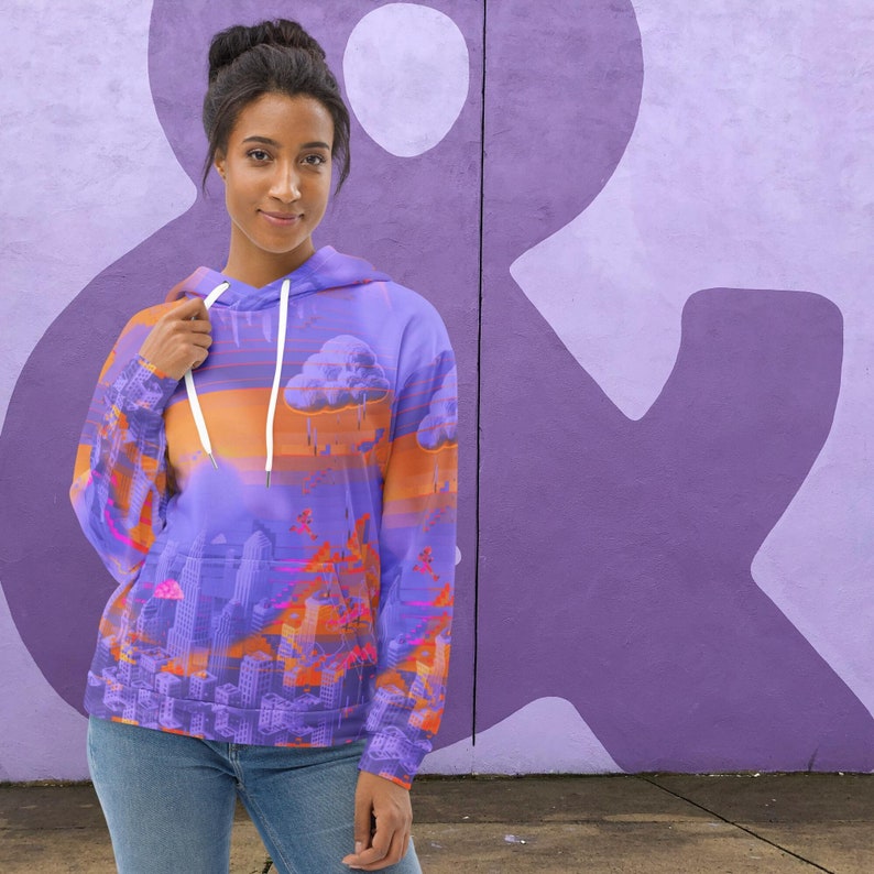 May include: A purple hoodie with a cityscape design featuring orange and pink accents. The hoodie has a drawstring and a hood. The background is a purple wall with a large white ampersand symbol.