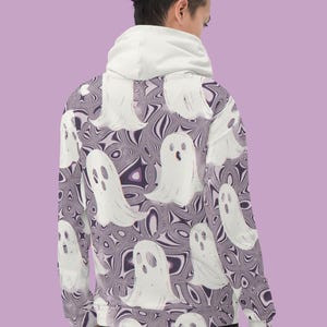 Puede incluir: Una sudadera con capucha blanca con un patr&oacute;n de fantasmas morados y blancos. La sudadera tiene una capucha con cord&oacute;n y mangas largas.