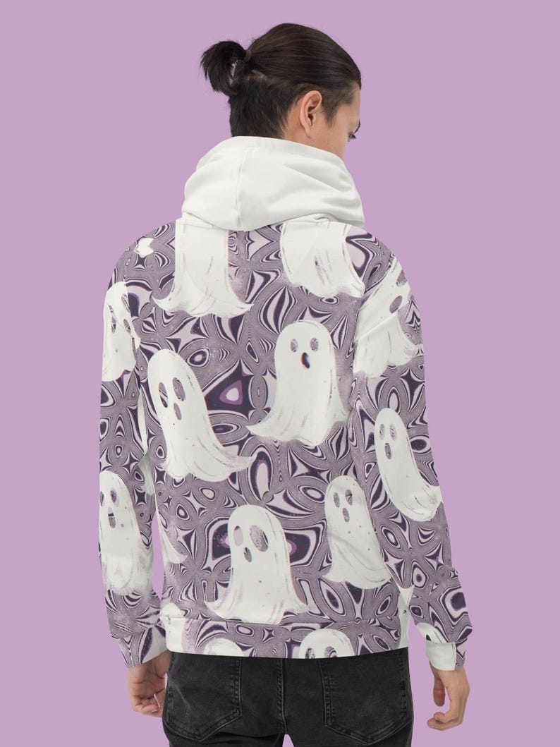 Puede incluir: Una sudadera con capucha blanca con un patr&oacute;n de fantasmas morados y blancos. La sudadera tiene una capucha con cord&oacute;n y mangas largas.