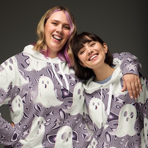 Puede incluir: Dos personas con sudaderas con capucha blancas con un patr&oacute;n de fantasmas morados y blancos. Las sudaderas tienen un cord&oacute;n blanco y un bolsillo canguro blanco.