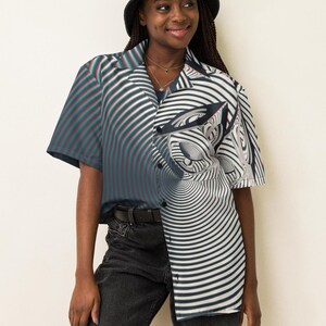 May include: A person wearing a black and white striped button-up shirt with a swirling pattern. The shirt has short sleeves and a collar. The person is also wearing a black bucket hat and black jeans.
