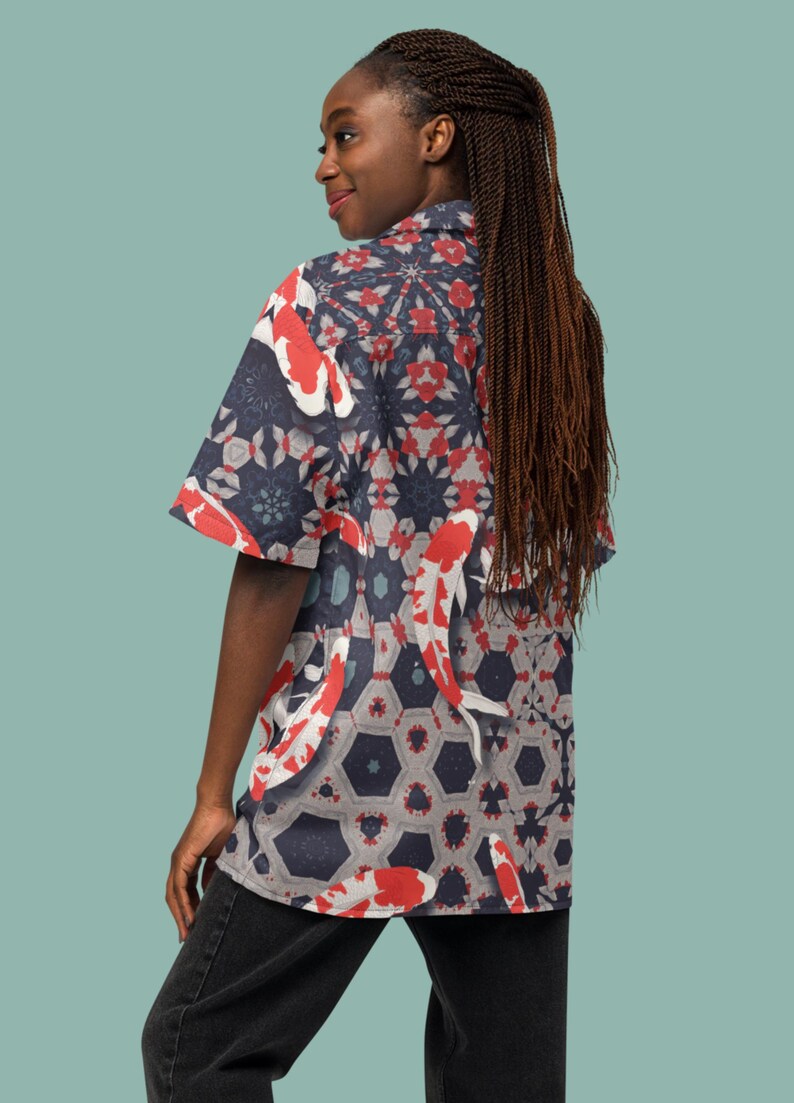 May include: Short-sleeved shirt with a koi carp pattern. The shirt has a navy blue background with red and white koi carp and geometric shapes. The shirt is worn by a person.