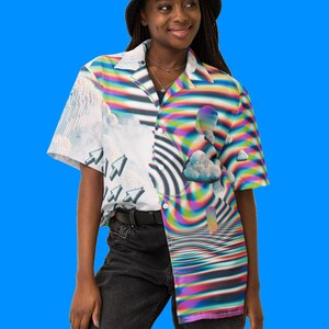 Puede incluir: Una persona lleva un sombrero de cubo negro y una camisa de manga corta con botones con un dise&ntilde;o colorido, abstracto y pixelado. La camisa presenta un patr&oacute;n de espiral de colores arco&iacute;ris y una nube con un halo de colores arco&iacute;ris.