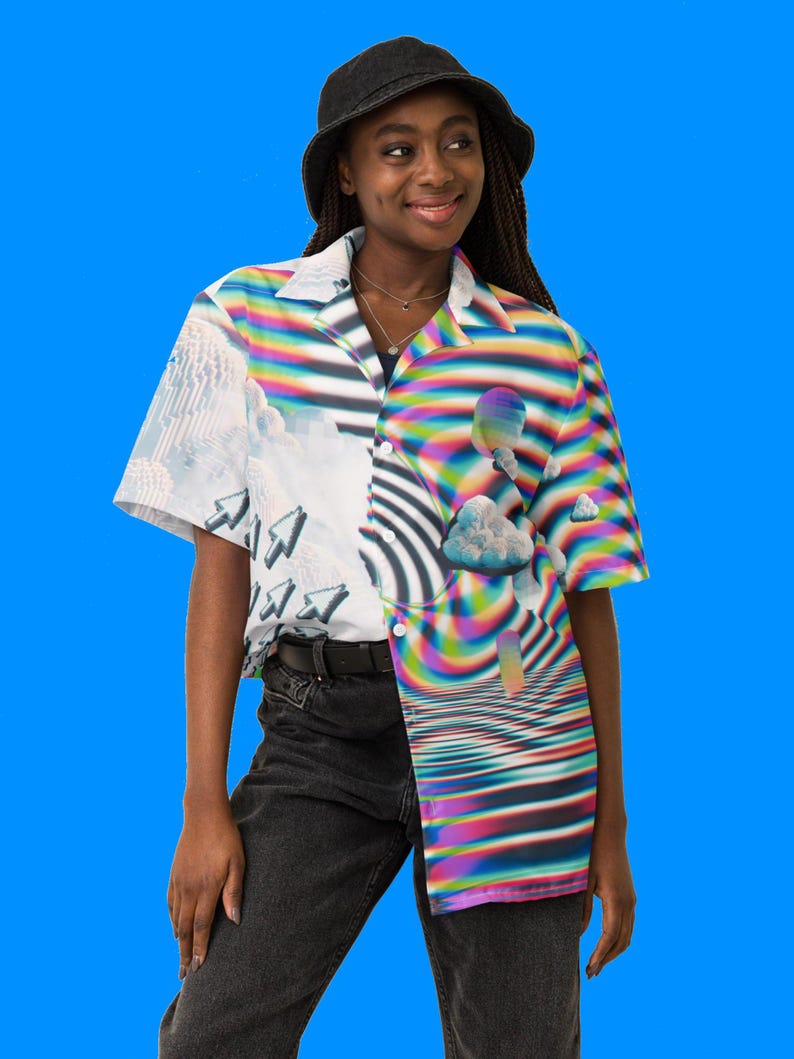 Puede incluir: Una persona lleva un sombrero de cubo negro y una camisa de manga corta con botones con un dise&ntilde;o colorido, abstracto y pixelado. La camisa presenta un patr&oacute;n de espiral de colores arco&iacute;ris y una nube con un halo de colores arco&iacute;ris.