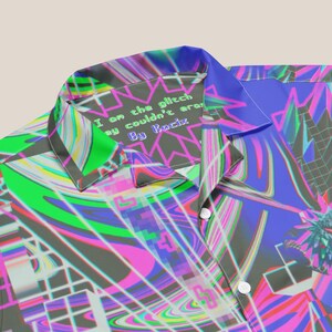 May include: A colorful button-up shirt with a psychedelic pattern. The collar has a black and white label with the text "I am the glitch they couldn't erase By Kocix".