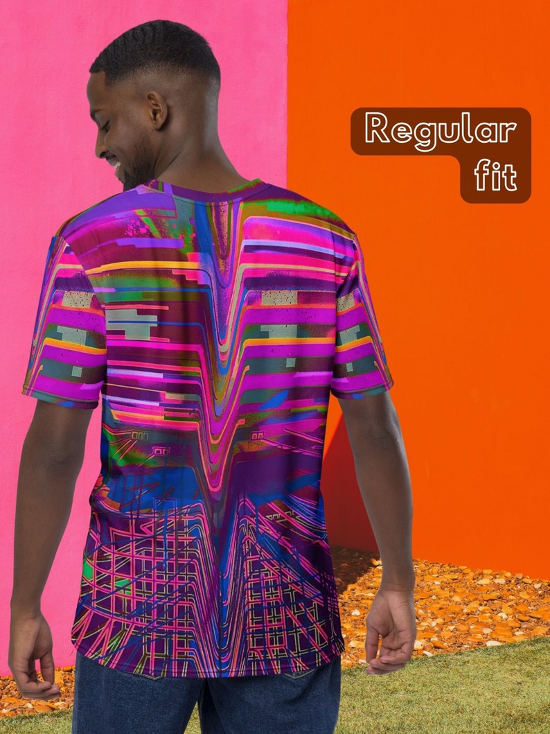 May include: A purple, pink, blue, and green abstract graphic print t-shirt with a regular fit. The t-shirt is being worn by a person standing in front of a pink and orange wall.