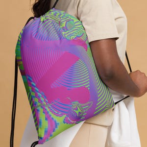 May include: A drawstring bag with a colourful abstract design featuring pink, green and blue lines and shapes. The bag has black drawstrings.