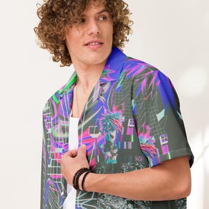 May include: A short-sleeved button-up shirt with a colorful, abstract print featuring geometric shapes, lines, and a pixelated figure. The shirt has a collar and a relaxed fit.