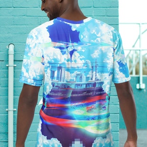Op de afbeelding: Een blauw, wit en paars T-shirt met een grafische print van een stadsbeeld, een trein en wolken. De grafiek heeft een gepixeld effect.