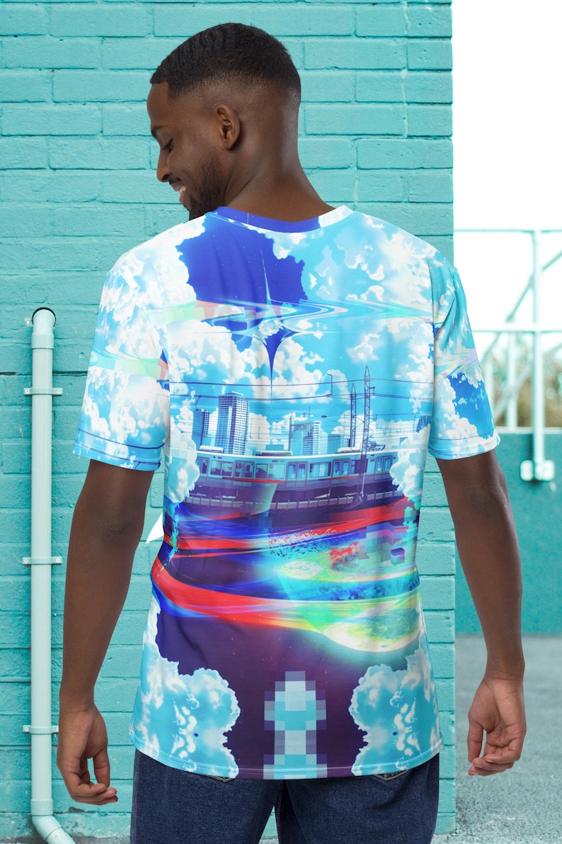 Op de afbeelding: Een blauw, wit en paars T-shirt met een grafische print van een stadsbeeld, een trein en wolken. De grafiek heeft een gepixeld effect.