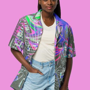 May include: A person wearing a short-sleeved button-up shirt with a colorful abstract print. The shirt has a blue, green, pink, and black design. The person is also wearing denim shorts.