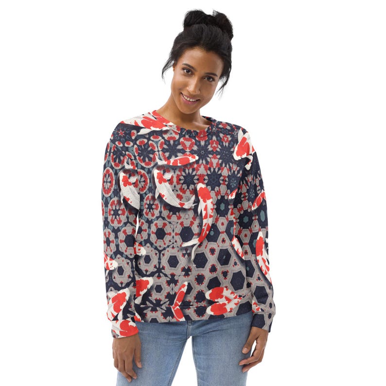 May include: A crew neck sweatshirt featuring a repeating pattern of koi fish in red, white, and gray against a navy blue background. The design incorporates geometric shapes and floral elements. The sweatshirt is worn by a person in blue jeans.