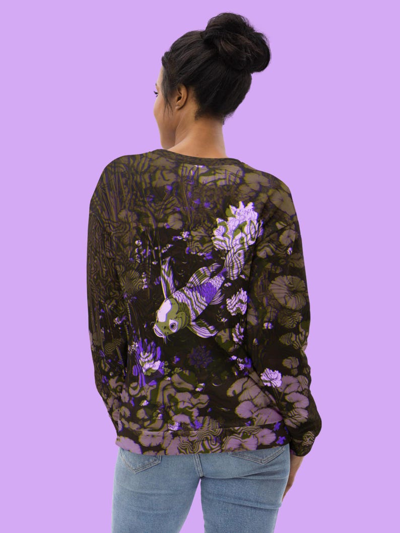 Puede incluir: Una sudadera negra con un estampado floral morado y verde con un pez koi blanco y morado. La sudadera tiene mangas largas y cuello redondo.