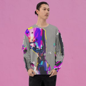 K&ouml;nnte beinhalten: Ein grauer Pullover mit einem farbenfrohen, abstrakten Design, das ein Frauen Gesicht, geometrische Formen und pixelige Elemente zeigt.