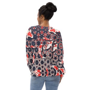 May include: A long-sleeved sweatshirt featuring a koi fish pattern. The design incorporates red, white, and black koi fish against a geometric background of gray, navy, and red shapes. The sweatshirt is worn by a person wearing blue jeans.