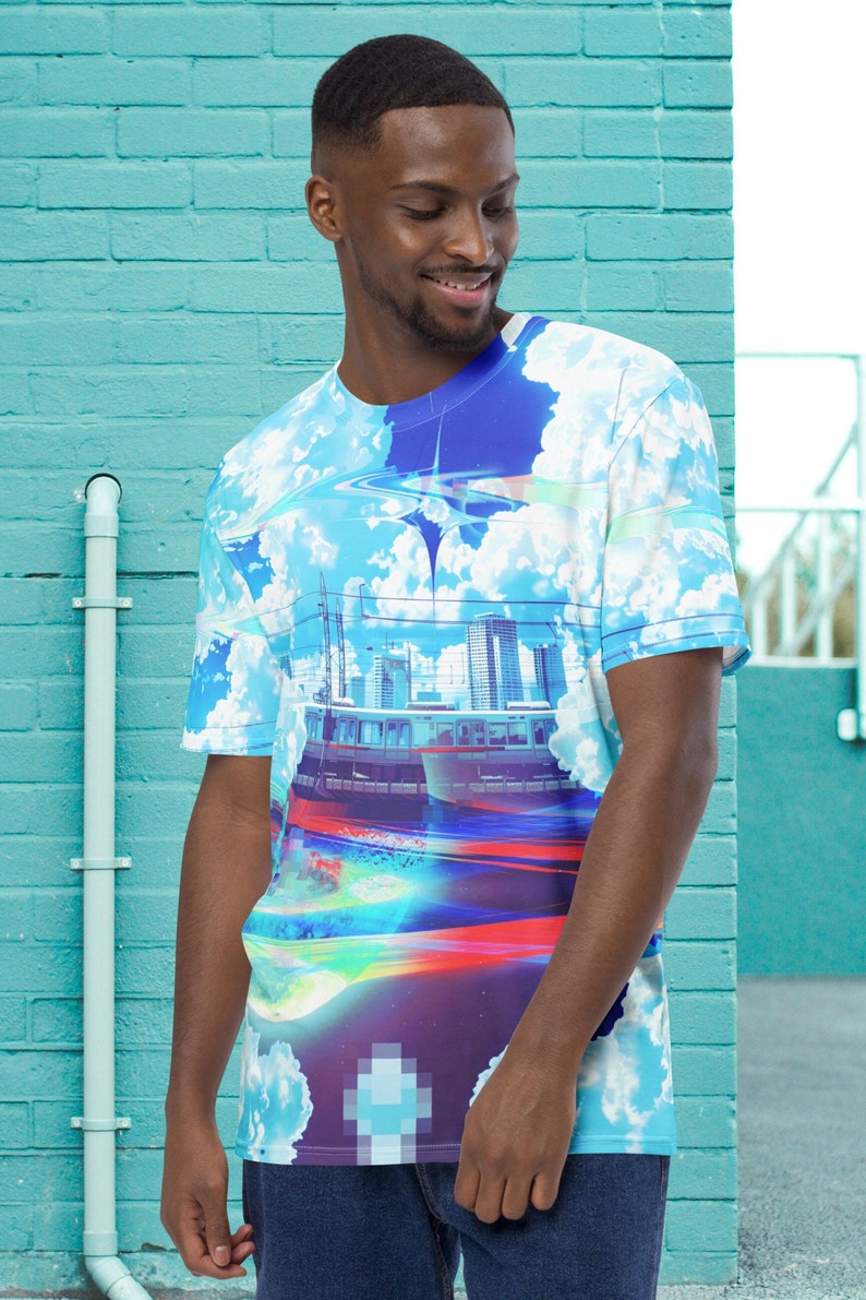 Op de afbeelding: Een blauw, wit en rood t-shirt met een stadsbeeld en wolken erop gedrukt. Het shirt heeft een ronde hals en korte mouwen.