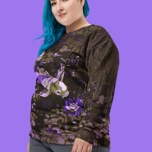 Puede incluir: Una sudadera negra con un estampado floral morado y verde que presenta un gran pez koi. La sudadera tiene mangas largas y cuello redondo.