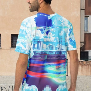 Op de afbeelding: Een blauw, wit en paars T-shirt met een grafische print van een stadsbeeld, wolken en een trein. De grafiek is een mix van gepixelde en realistische elementen.