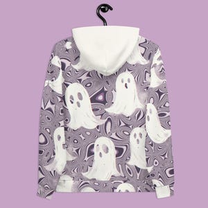Puede incluir: Una sudadera con capucha de color morado y blanco con un patr&oacute;n de remolino y siluetas de fantasmas blancos. La sudadera tiene una capucha blanca.