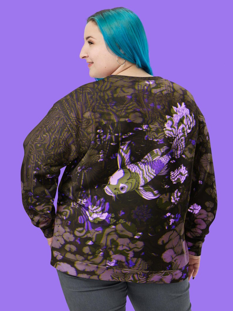 Puede incluir: Una sudadera negra con un estampado floral morado y verde que presenta un gran pez koi. El pez nada en un estanque con nen&uacute;fares y otras plantas acu&aacute;ticas.