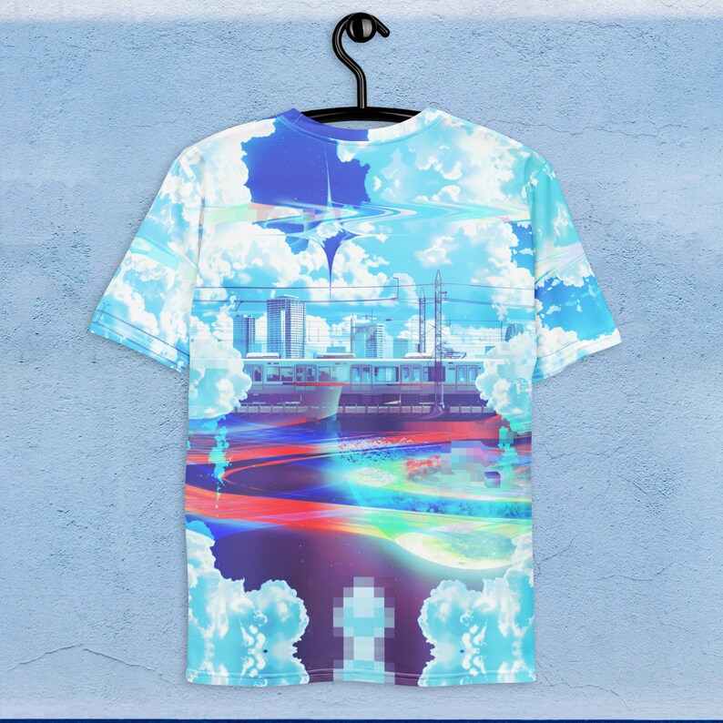 Op de afbeelding: Een blauw, wit en paars T-shirt met een grafische print van een skyline van een stad, een trein en een draaiende galaxie. Het ontwerp doet denken aan een futuristisch stadsbeeld.