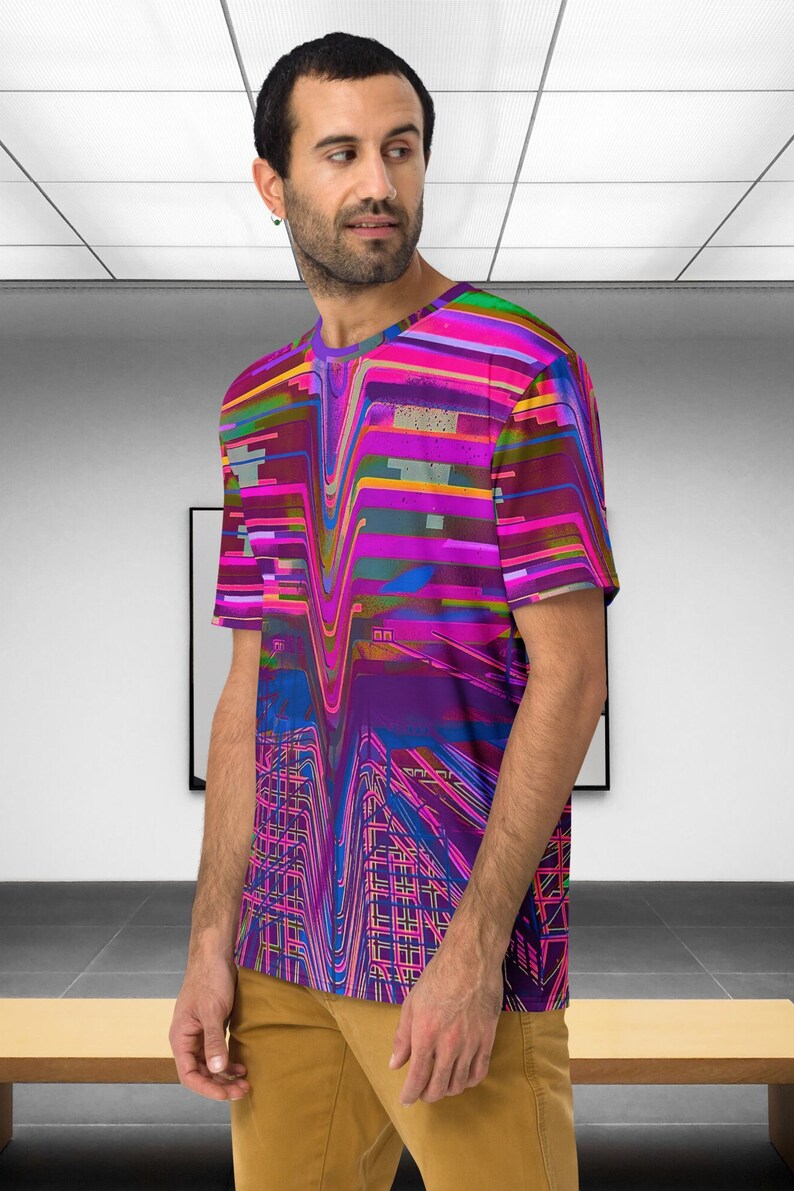 May include: A man wearing a short-sleeved t-shirt with a colorful abstract design. The design features a mix of pink, purple, blue, and yellow lines and shapes.