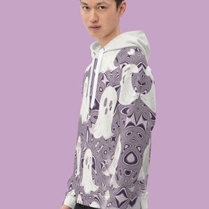 Puede incluir: Una sudadera con capucha blanca con un patr&oacute;n de fantasmas morados y blancos. La sudadera tiene una cremallera y una capucha.