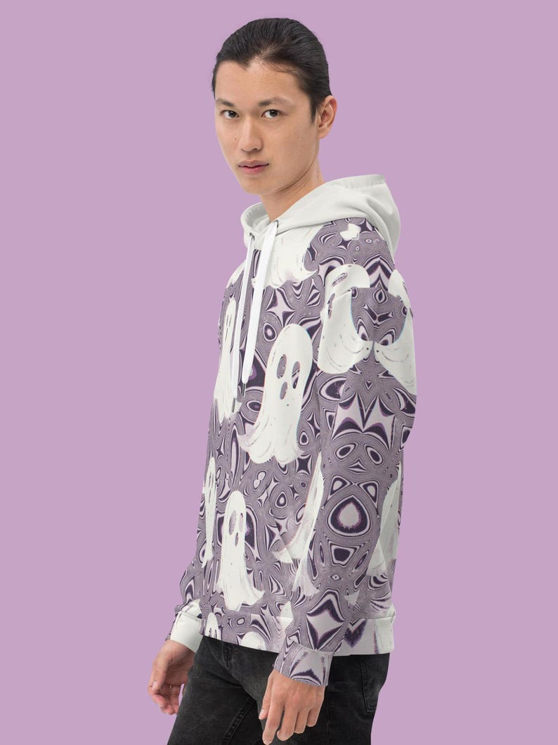 Puede incluir: Una sudadera con capucha blanca con un patr&oacute;n de fantasmas morados y blancos. La sudadera tiene una cremallera y una capucha.
