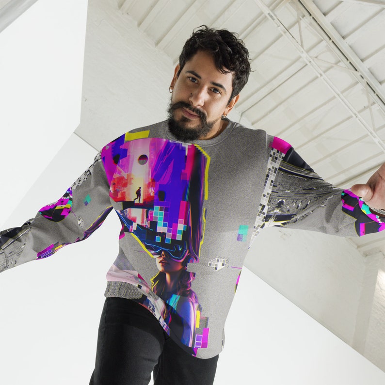 K&ouml;nnte beinhalten: Ein graues Sweatshirt mit einem bunten, pixeligen Design, das eine Frau mit einer Virtual-Reality-Brille zeigt. Das Design beinhaltet auch eine Person, die in einer futuristischen Landschaft geht.
