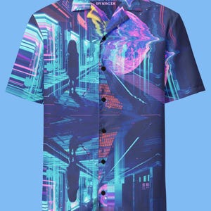 May include: A blue short-sleeved button-down shirt with a colorful, abstract print of a city scene. The print features a person walking through a neon-lit city with a large, swirling orb in the background. The shirt has a collar and a button closure. The text "DON'T GET PLAY FOR BY KACIX" is printed on the collar.
