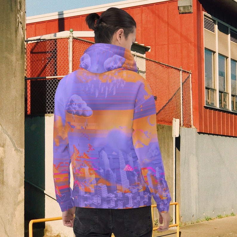 May include: A purple hoodie with an abstract cityscape design. The design features a sunset with orange and purple hues, clouds, and a city skyline. The hoodie is made of a soft material.