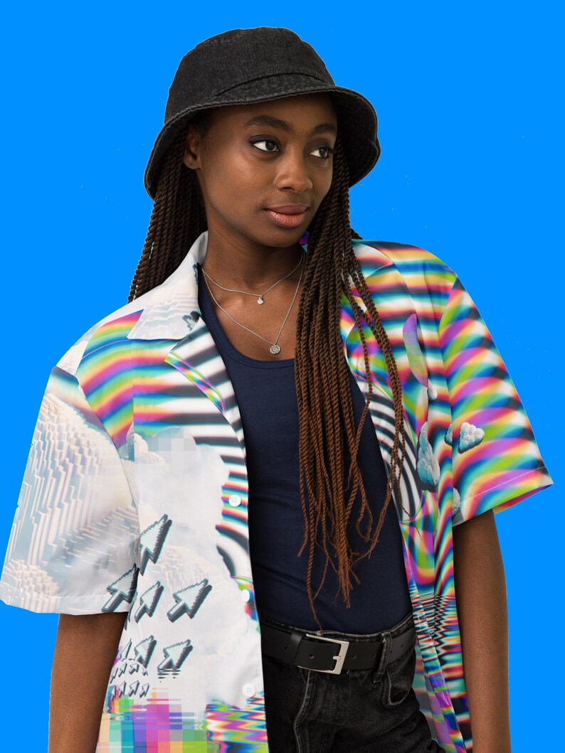 Puede incluir: Una persona lleva una camisa blanca abotonada con un dise&ntilde;o colorido, pixelado y abstracto. La camisa tiene mangas cortas y cuello. La persona tambi&eacute;n lleva un sombrero de pescador negro y pantalones vaqueros negros.
