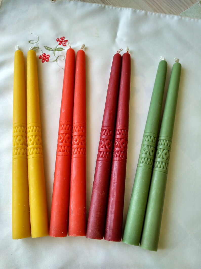 Op de afbeelding: Zes taps-kaarsen in geel, rood en groen. De kaarsen zijn versierd met een herhalend geometrisch patroon.