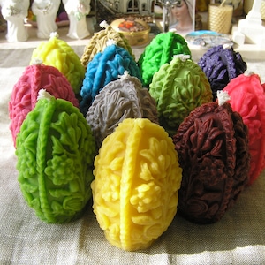 May include: A collection of intricately carved, colourful beeswax candles shaped like eggs. The candles are arranged in a circle on a white linen tablecloth.