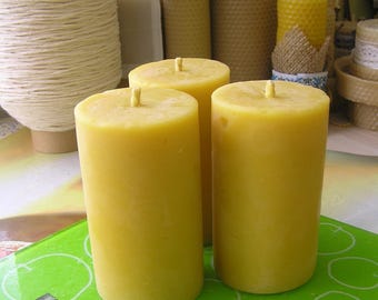 May include: Three yellow beeswax candles on a green digital kitchen scale. The candles are cylindrical and have a smooth surface. The scale has a digital display and a unit button.