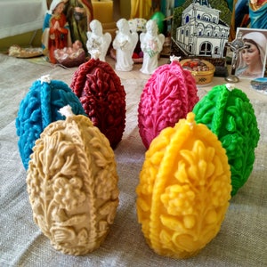 May include: Six intricately carved, colourful beeswax candles shaped like eggs. The candles are arranged in a circle on a linen tablecloth.