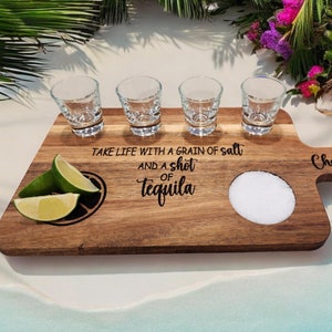 May include: Wooden serving board with four shot glasses, a lime wedge, and a salt dish. The board has the text "Take life with a grain of salt and a shot of tequila" and "Cheers" engraved on it.