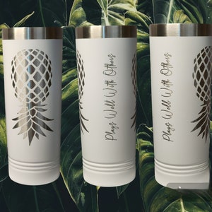 May include: A white ceramic mug with a black handle and the text "But First, Coffee" in a bold, black font. The mug is set against a blurred background, suggesting a cozy setting.