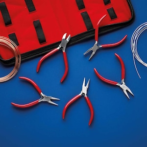 May include: A selection of jewellery-making tools and supplies, including red-handled pliers, spools of copper wire, and a red tool case, arranged on a blue surface. The pliers have silver metal heads.