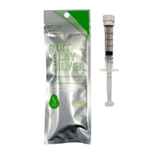 May include: A silver-colored foil packet labeled ART CLAY SILVER with a green accent and a 5g weight indicator, accompanied by a clear plastic syringe applicator with a white cap and black measurement markings along the side of the barrel.