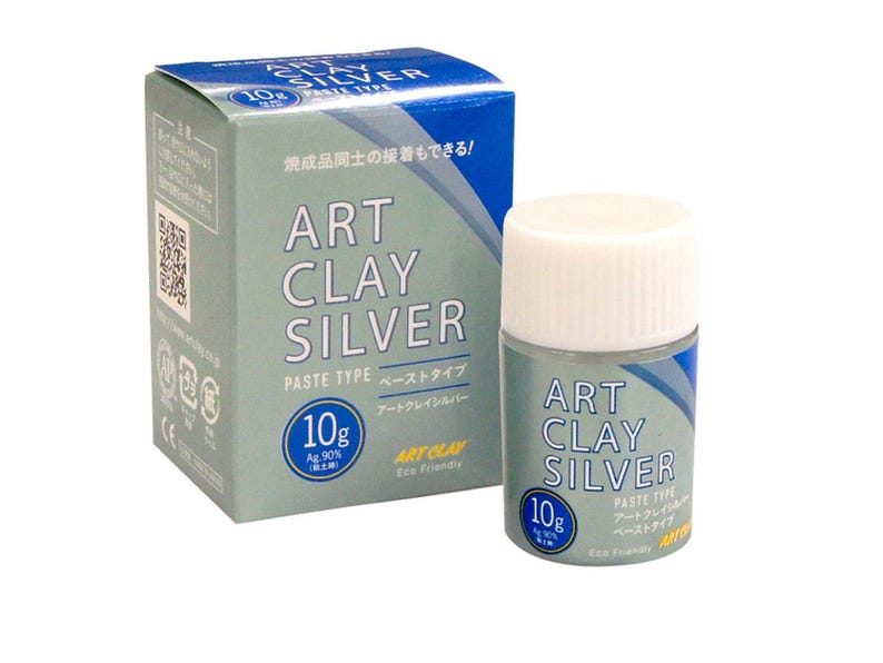 May include: A 10g container of Art Clay Silver paste type and its matching cardboard box. The packaging is light blue and white with the text Art Clay Silver, 10g, and Ag 90% printed on the front. The container has a white screw-on cap.