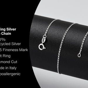 May include: A sterling silver curb chain with a bolt ring clasp, displayed on a black surface. The chain is diamond cut and made in Italy. Text on the left indicates it is 100% recycled silver and hypoallergenic.