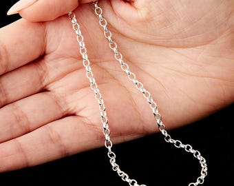 May include: A fine silver chain necklace featuring small, circular links. The necklace is displayed against a hand, highlighting its simple and elegant design. The chain has a bright, polished silver appearance.
